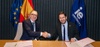 Two men are shaking hands in a formal setting, with flags in the background.