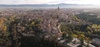 Aerial view of a historic European city with a large cathedral dominating the skyline, surrounded by autumn-colored trees and old buildings.