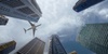 A plane flying above tall skyscrapers under a cloudy sky.