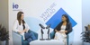 Two women are seated in a professional discussion setting with microphones.