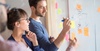 Two professionals brainstorming with sticky notes on a glass wall.
