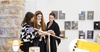 Three women examining documents in an art gallery with photos displayed on the wall.