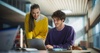 Two young people collaborate on a laptop in a modern workspace.