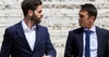 Two men in suits having a conversation against a textured wall.