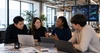 A group of four professionals discussing ideas around a table in a modern office environment.