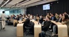 A group of people sitting in a modern classroom listening to a presenter at the front.