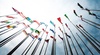A collection of various national flags fluttering on poles against a blue sky with white clouds.