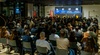 A large audience gathered in a conference setting with a panel discussion on stage.