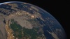 A view of Earth from space showing part of a continent illuminated by city lights under a dusky sky.