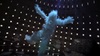 A figure made of clouds is suspended in a circular, dimly lit space with multiple windows.