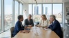 A group of four professionals engaged in a discussion around a conference table with a city skyline visible through large windows.