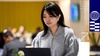 A woman is focused on working on her laptop in a busy office setting.