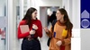 Two young women happily conversing while walking through a school corridor, one holding a notebook and the other a cup.