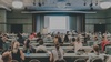 A large audience attending a presentation in a conference room.
