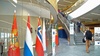An interior view of a modern building featuring flags and people walking up the stairs.