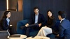 Four business professionals are sitting and engaging in a conversation in a modern office lounge.