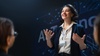 A woman is enthusiastically presenting in front of an audience at a technology conference.