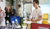 A young man demonstrates a robotic drone in a modern tech environment with various humanoid robots on display.