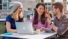 Three IE students speaking outside sitting on a table with a computer