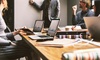 A group of professionals are engaged in a business meeting around a wooden table with laptops and documents.