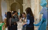 A group of young women engaging in a conversation at a public event, with a cartoon character in the background.