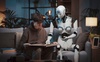 A young person is reading a book while a humanoid robot assists them.