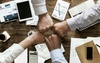Four people fist bumping over a busy meeting table filled with electronic devices, documents, and coffee cups.