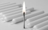A lit matchstick stands out among a row of unlit white candles.