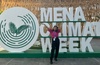 A person posing in front of a large sign that reads 'MENA Climate Week' with a circular logo featuring a palm design.