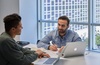 Two men are engaged in a discussion over a laptop at a table.