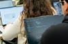 A student is coding on a laptop while another student works in the background.