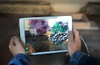 A person holding a tablet displaying colorful, animated 3D objects in a creative setting.