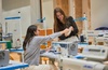 Two women are engaged in a sewing activity at a well-equipped workspace.