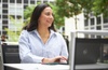 A woman smiling while working on her laptop outdoors.