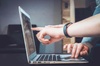 A person pointing at a laptop screen while another person watches.