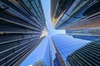 A dynamic upward view of towering skyscrapers converging into a clear blue sky.