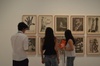 A group of people examining various framed artworks displayed on a gallery wall.