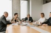 A group of five professionals in a meeting around a table in a modern office setting.
