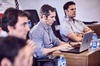 A group of men focused on laptops and listening during a business meeting in a modern office.