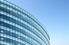 A modern building with a curved glass facade reflecting the clear blue sky.