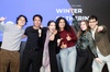 A group of six young adults are joyfully posing together at an event, with a background banner reading 'IE Foundation Fellows Winner Gathering December'.