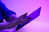 A person using a laptop in a room illuminated by purple light.