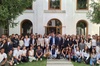 A large group of students posing for a photo with a few adults in front of a building with a classic facade and green lawn.