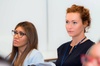 Two women attentively participating in a seminar, one with auburn hair and the other wearing glasses.