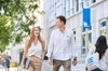 Two young adults walking and laughing together on a university campus, one of them holding books.