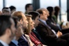 A group of people sitting in a row at a conference, focused attentively forward.