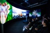 People sitting in a dark room watching a panoramic display showing vibrant images of nature and cities.