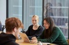 Three young adults are engaged in a discussion around a laptop at a table.