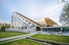 Modern architectural building featuring an angular design and a predominantly white facade, surrounded by a green lawn and a pedestrian walkway.