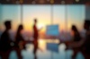A silhouette of a person presenting in a conference room with a city skyline at sunset in the background.